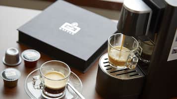 Una cafetera, una taza de vidrio con café, una caja y dos pequeños recipientes sobre una mesa de madera.
