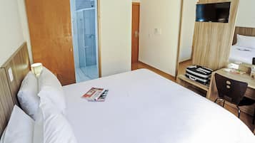 Habitación de hotel con cama, escritorio, silla, televisor y baño con ducha.