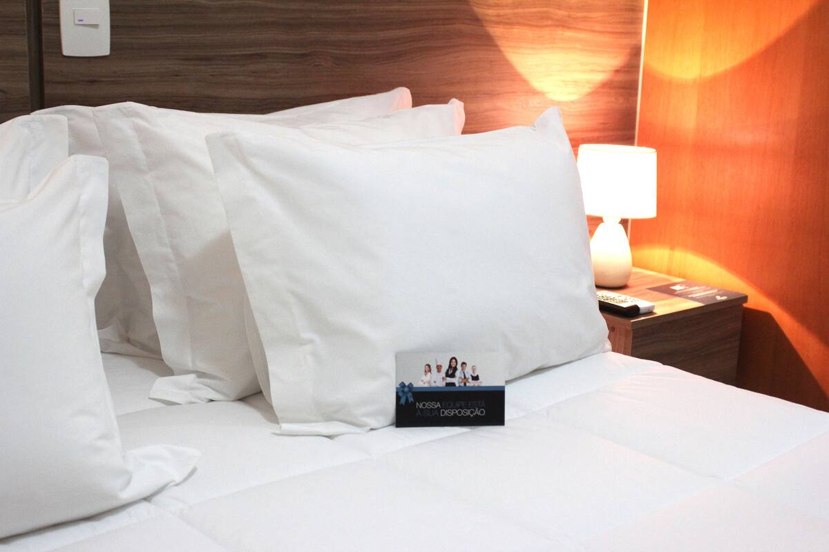 A neatly made bed with white linens, a bedside lamp, and a small card on the nightstand.