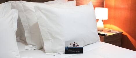 A neatly made bed with white linens, a bedside lamp, and a small card on the nightstand.