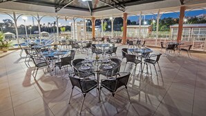 A covered outdoor dining area with multiple tables and chairs, large windows, and a view of the cityscape. - The Hill Executive (São Carlos)