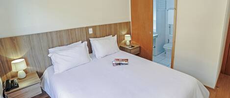 Habitación de hotel con una cama grande, una mesita de noche con lámpara, teléfono y una revista.