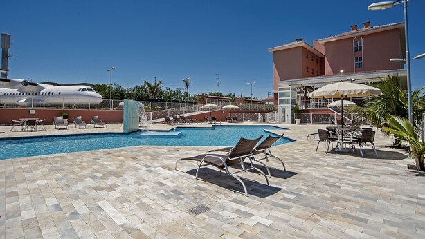 A pool area with lounge chairs, a swimming pool, and a building in the background. - The Hill Executive (São Carlos)