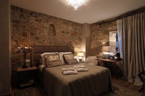 A bedroom with a stone wall, a bed with towels, a nightstand, a lamp, and a desk with a lamp. - Casa Granados Boutique Hotel (Tossa de Mar)