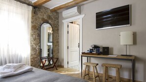 A bedroom with a bed, a desk with a chair, a mirror, and a TV on the wall. - Casa Granados Boutique Hotel (Tossa de Mar)
