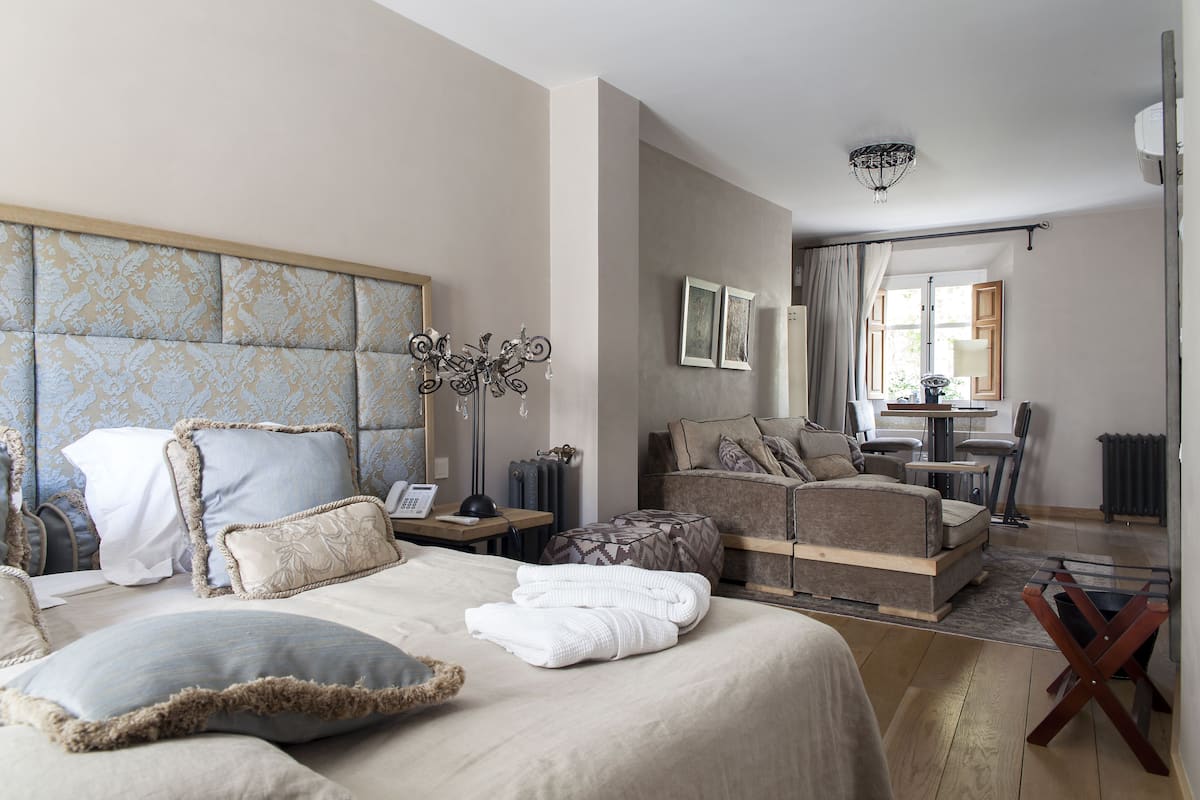 A hotel room with a large bed, a sofa, a desk with a lamp, and a view of the outside.