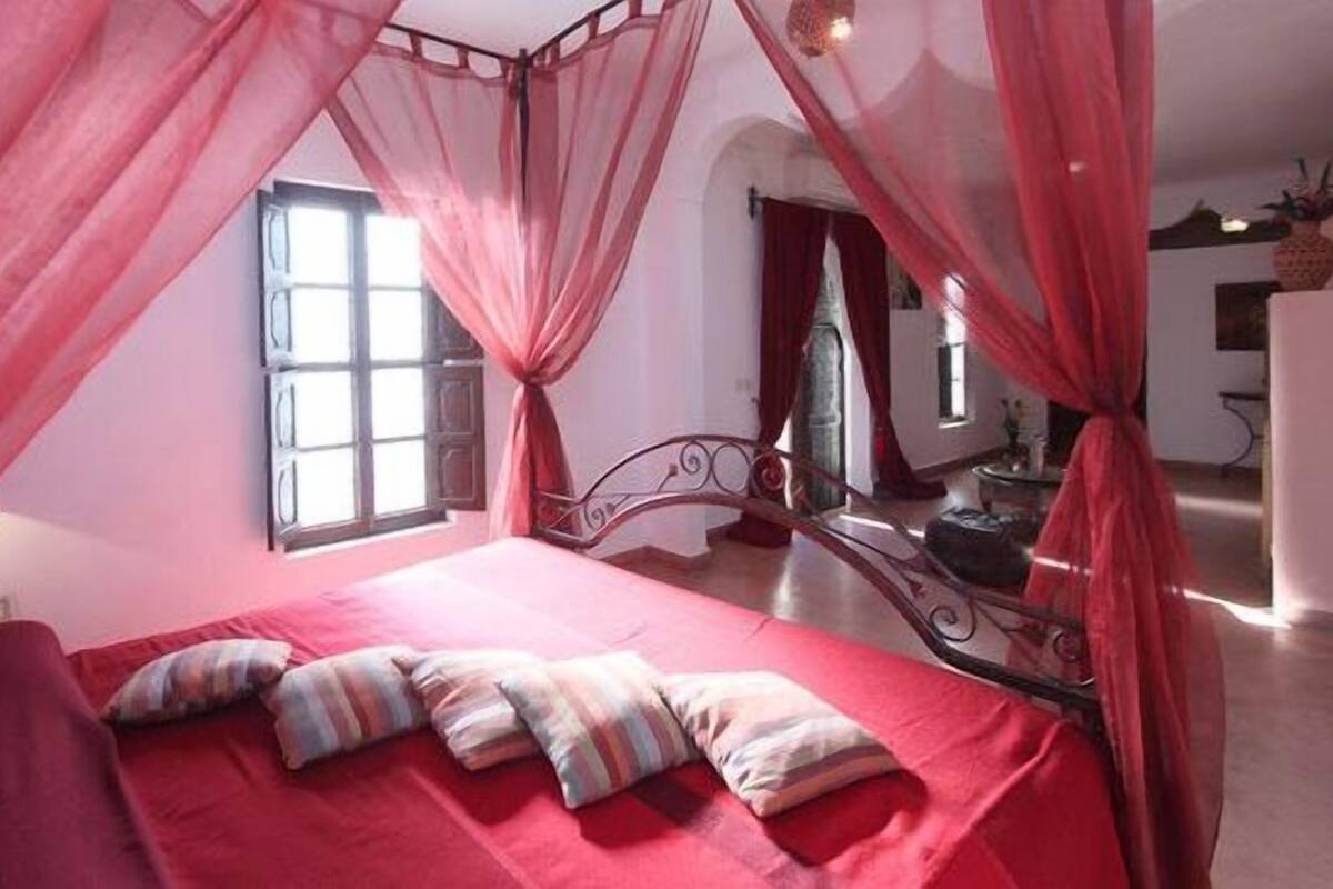 A bedroom with a four-poster bed, red bedding, and a canopy.