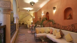 A hotel lobby with a staircase, a sofa with cushions, a table, and decorative wall sconces. - Riad Sidi Ayoub (Marrakech)