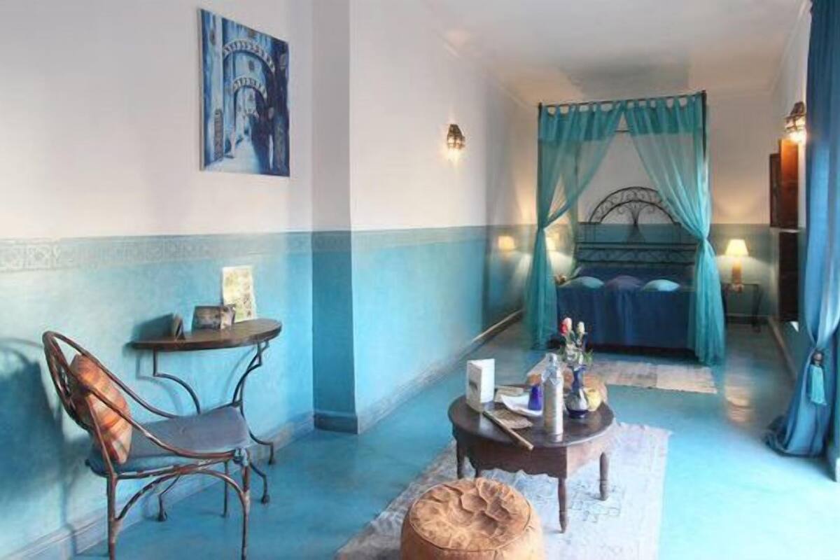 A bedroom with a bed, a chair, a small table, and a nightstand.