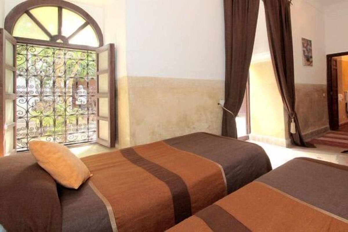 A room with two beds, a window with a metal gate, and a door leading to another room.