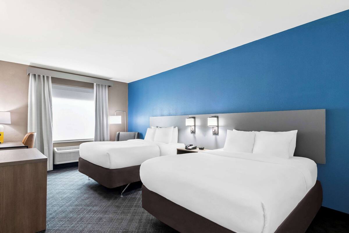 Une chambre d’hôtel avec deux lits, un bureau, une lampe et une fenêtre avec des rideaux.