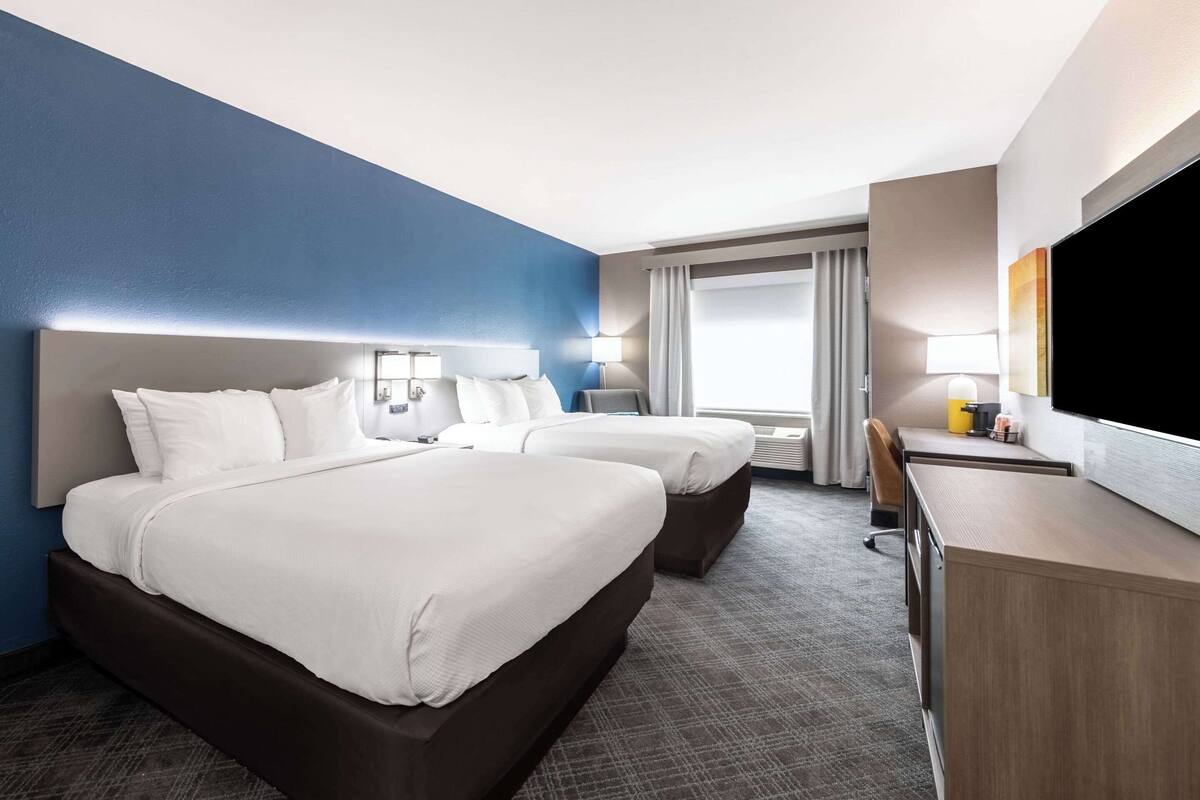 Une chambre d’hôtel avec deux lits, un bureau, une télévision et une fenêtre avec des rideaux.