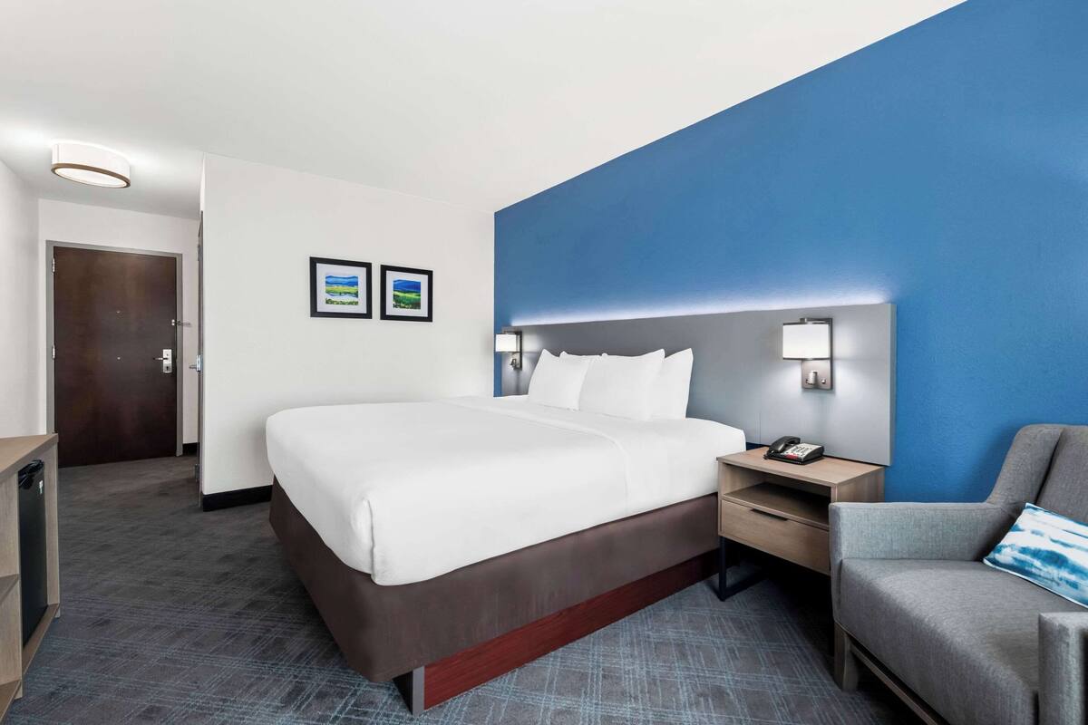 Une chambre d’hôtel avec un grand lit, un bureau avec un téléphone, une chaise et une table de chevet avec une lampe.
