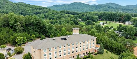 A multi-story hotel with a flat roof, surrounded by lush greenery and hills.