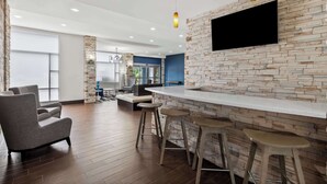 Un área de bar moderna con pared de piedra, un televisor de pantalla plana y taburetes de bar.