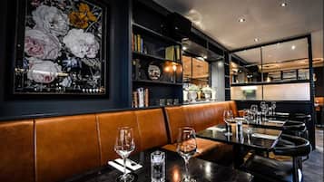 L’intérieur d’un restaurant présente une décoration aux couleurs sombres, des sièges en cuir et une grande œuvre d’art florale accrochée au mur.
