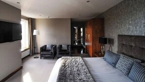 Una habitación de hotel moderna con una cama grande, dos sillones, un televisor de pantalla plana y una pared de acento de piedra.