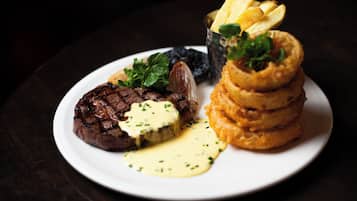 A plate of food with steak, onion rings, and a small cup of sauce.