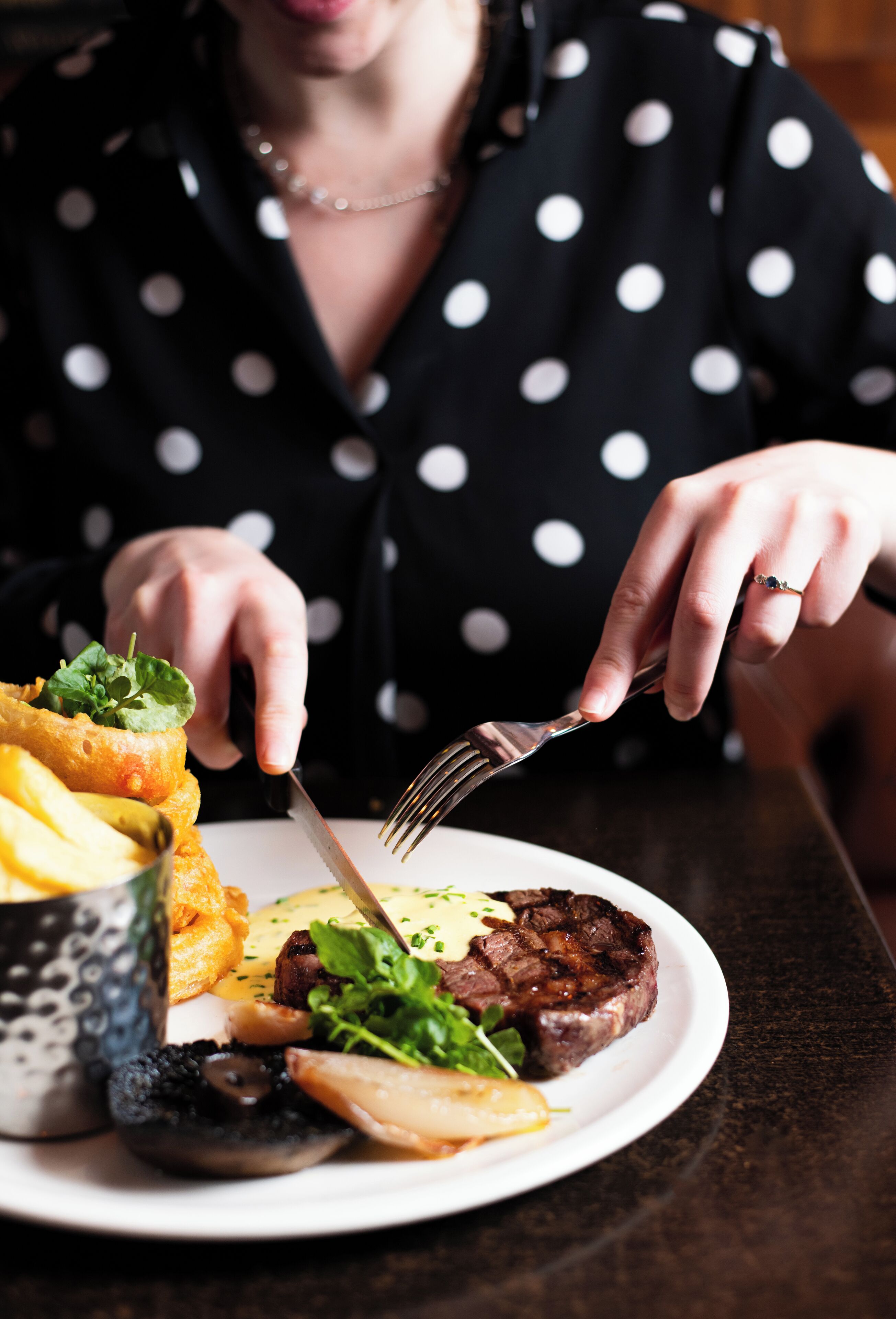 Une personne est assise à une table et prend son repas. Son assiette contient un steak, des pommes de terre et des légumes verts.