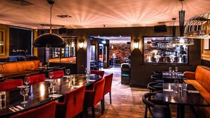 Un restaurante con mesas de madera, sillas rojas y una zona de bar con estantes llenos de botellas.