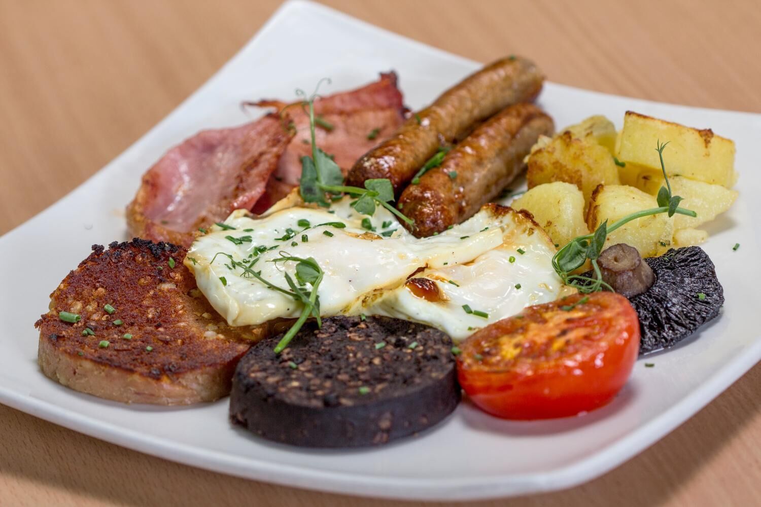 A plate of breakfast food including sausages, eggs, potatoes, and tomatoes.