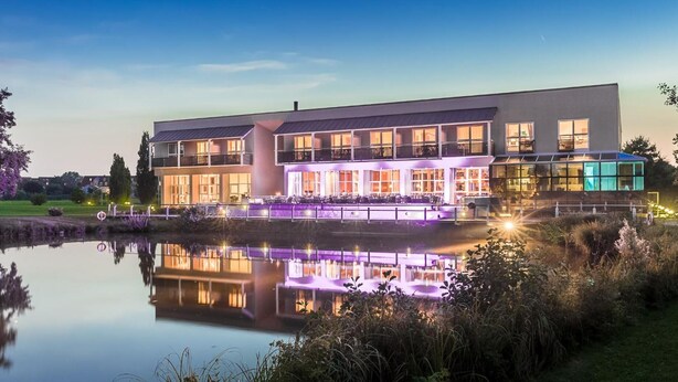 A modern building with a reflective pool in front, featuring a large balcony and outdoor seating area. - Golfhotel & Restaurant Lindenhof (Bad Vilbel)