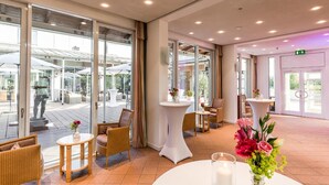 A hotel lobby with wicker furniture, a white round table with a candle, and a vase of flowers. - Golfhotel & Restaurant Lindenhof (Bad Vilbel)