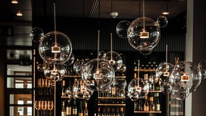 A restaurant interior with round tables, brown chairs, and a wine rack in the background. - Golfhotel & Restaurant Lindenhof (Bad Vilbel)