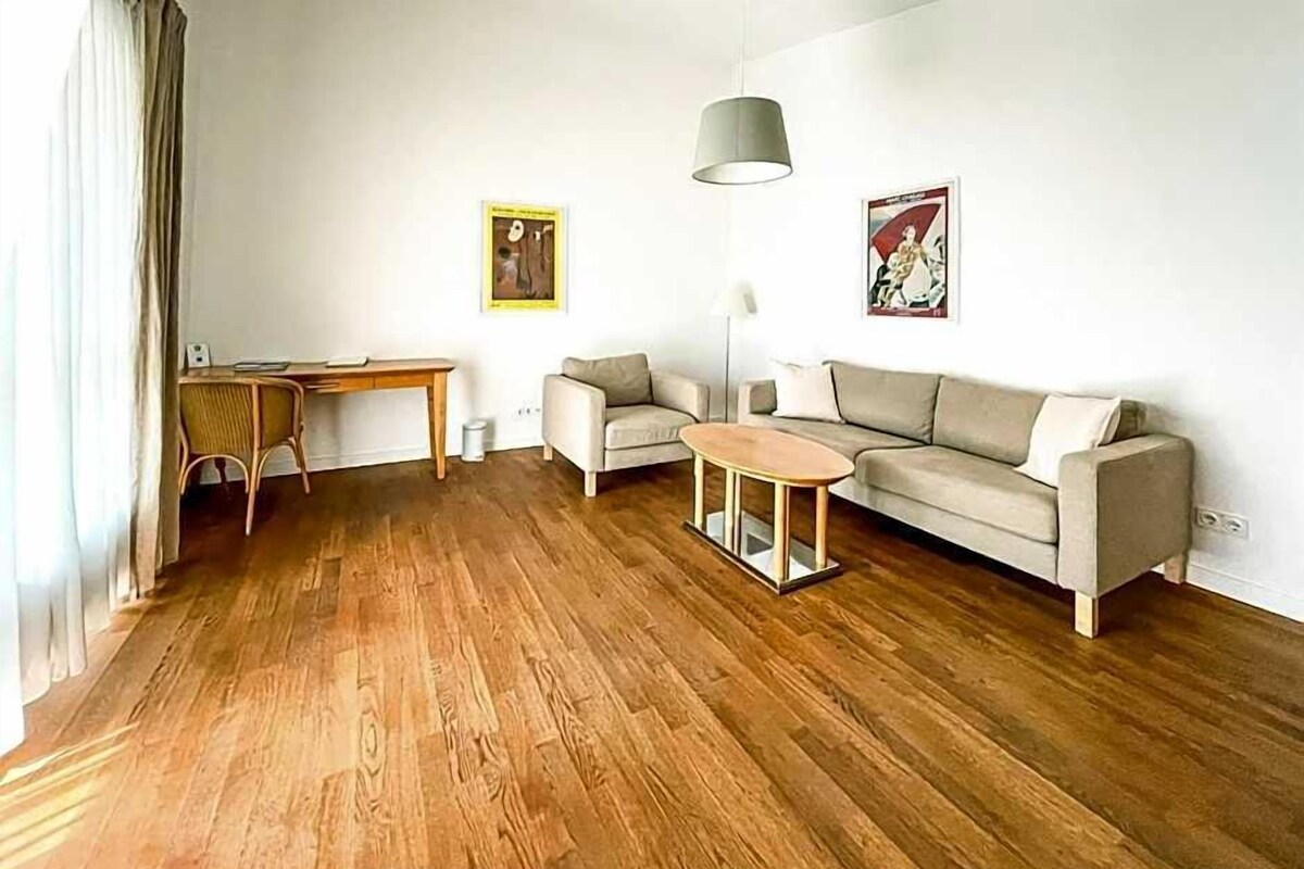 Een woonkamer met een houten vloer, een bank, een bijzettafeltje, een lamp en twee foto's aan de muur.