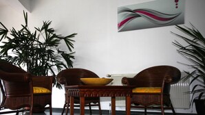 A room with two wooden chairs with yellow cushions, a wooden table with a bowl, and a large potted plant. - Hotel Antares (Halberstadt)