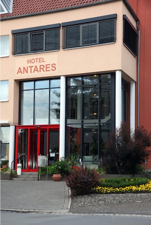 A hotel with a red entrance, large windows, and a sign reading "HOTEL ANTARES". - Hotel Antares (Halberstadt)