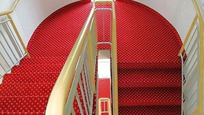 A staircase with red carpeted steps and a yellow handrail. - Hotel Antares (Halberstadt)