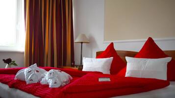 Una habitación de hotel con una cama cubierta con un edredón rojo, almohadas blancas y una rosa roja en un jarrón.