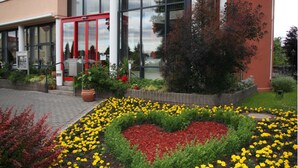A building entrance with a glass door, a heart-shaped flower bed, and a small garden area. - Hotel Antares (Halberstadt)
