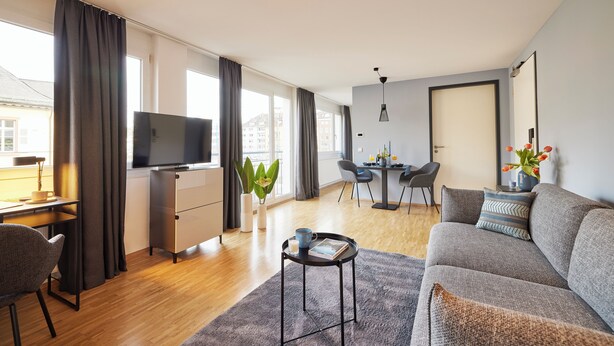Een moderne woonkamer met een bank, salontafel, televisie en een eethoek met tafel en stoelen.
