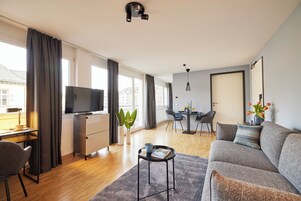 A modern living room with a sofa, a coffee table, a TV, and a dining area with a table and chairs.