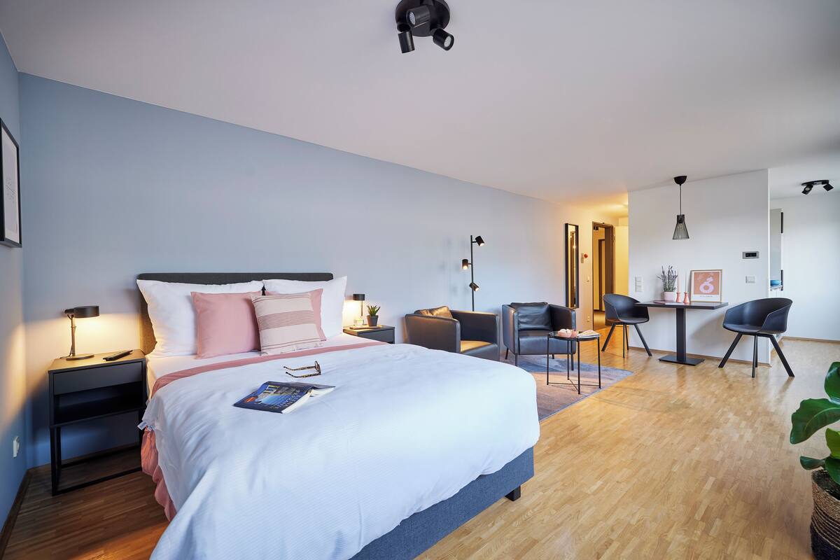 Een moderne hotelkamer met een groot bed, nachtkastjes, een bureau, twee stoelen en een kleine tafel met een plant.