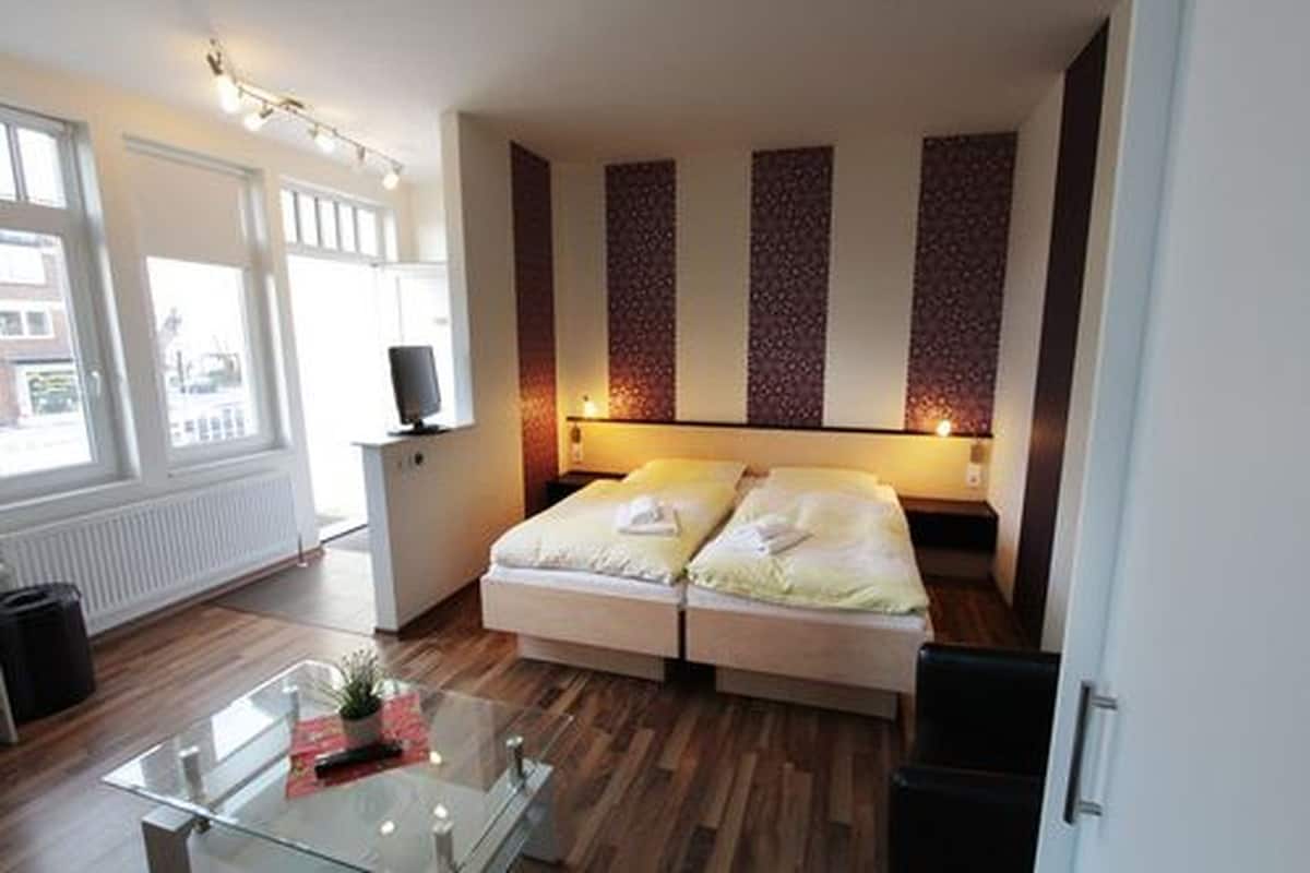 A hotel room with a bed, a small desk, a glass table, and a view of the outside.