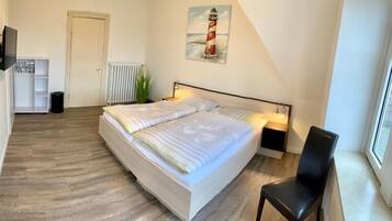A bedroom with a bed, bedside tables, a chair, a radiator, a door, and a painting of a lighthouse.