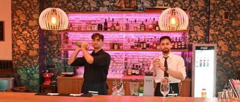 A bar area with two bartenders, a brick wall with shelves of bottles, and a Coca-Cola refrigerator.