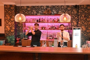 A bar area with two bartenders, a brick wall with shelves of bottles, and a Coca-Cola refrigerator. - Gästehaus Seewarte (Flensburg)