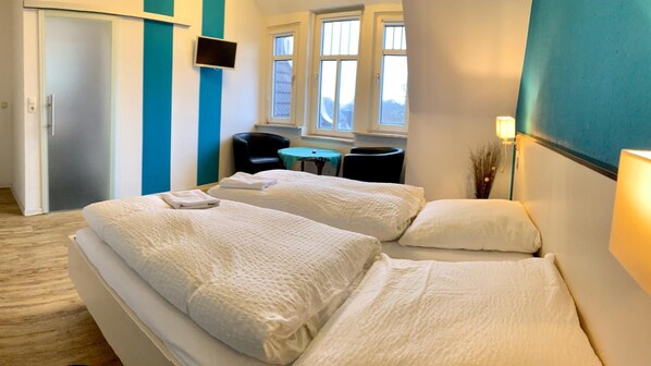 Habitación de hotel con dos camas, televisión, una silla, una mesita y ventanas con vistas.