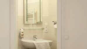 Un baño con un lavamanos blanco, estante de vidrio, espejo y toallero.