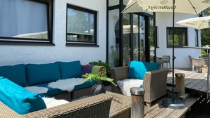 An outdoor seating area with wicker furniture, a white wall, and large windows.