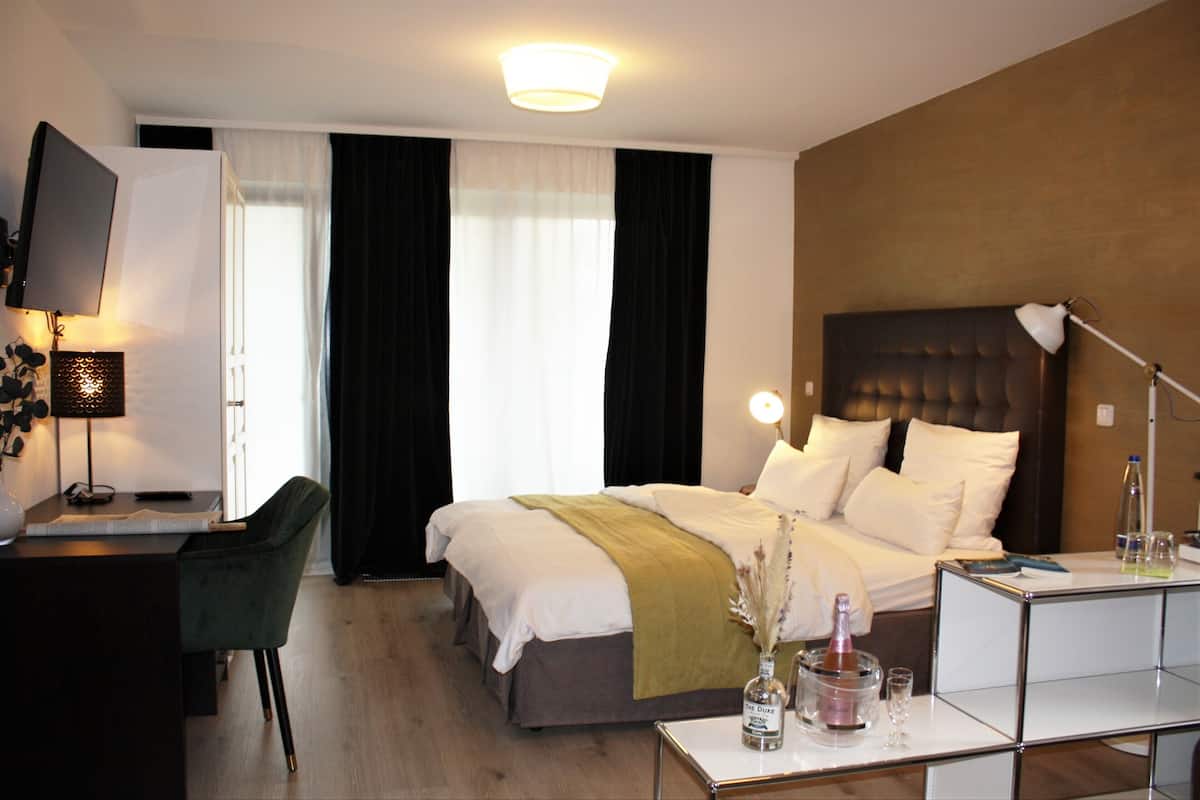 Habitación de hotel con cama, mesita de noche, escritorio, silla y televisor montado en la pared.