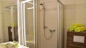 Ein modernes Badezimmer mit einer gläsernen Duschkabine, einem Holzkosmetikschrank und ordentlich gefalteten Handtüchern.