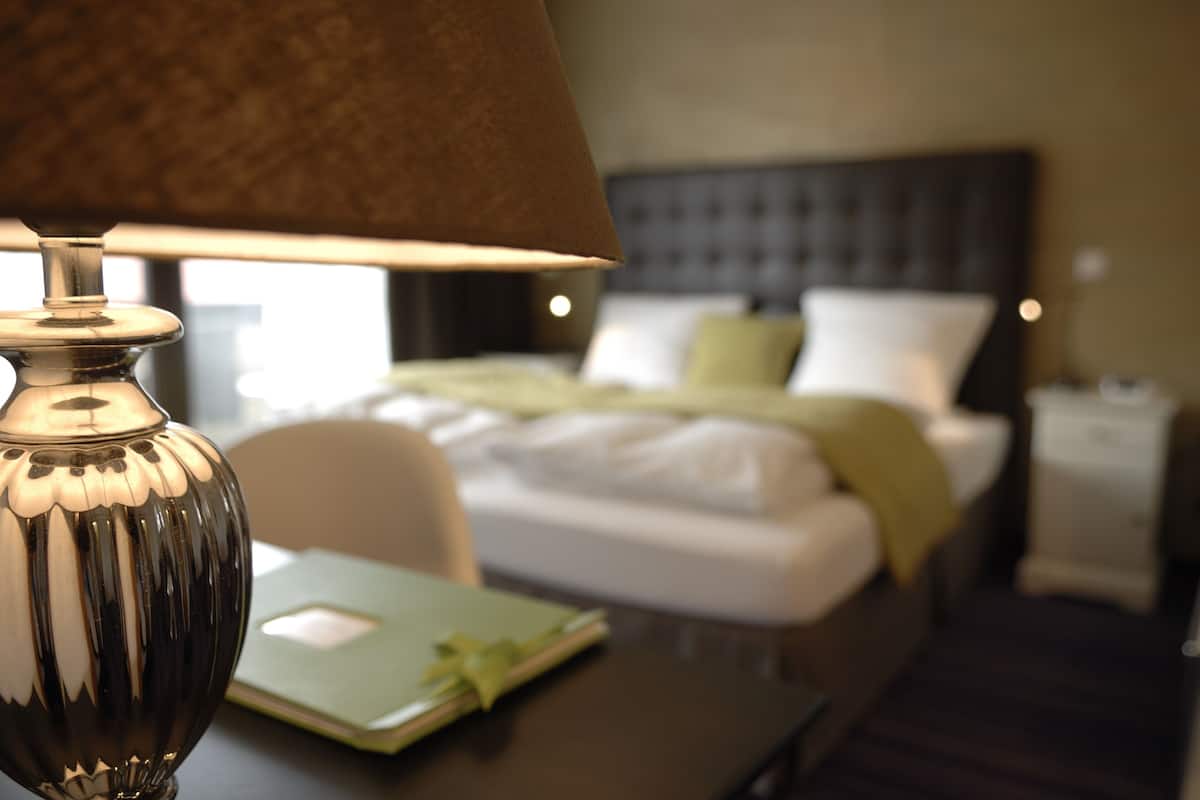 Habitación de hotel con una cama, una mesita de noche con lámpara y una carpeta verde sobre la mesa.