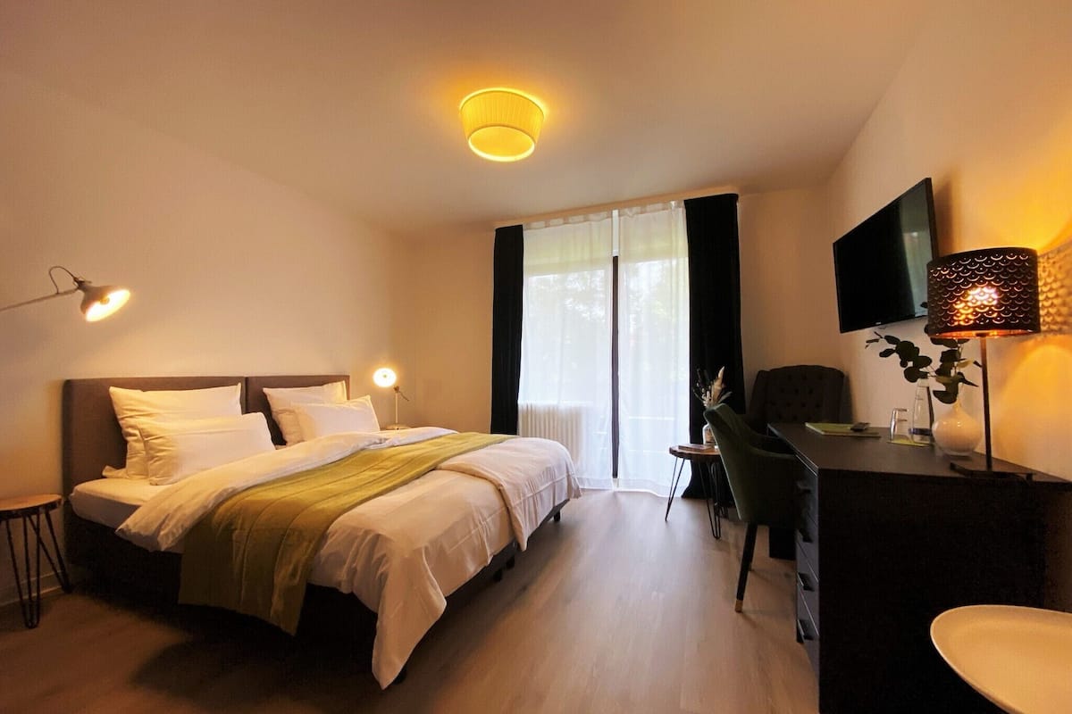 Habitación de hotel con cama, escritorio, silla, televisor y lámpara.