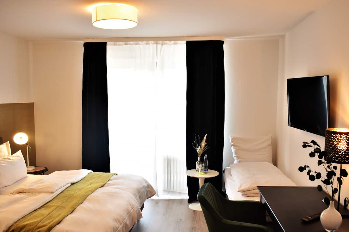 Habitación de hotel con dos camas, un escritorio, un televisor y una mesita con un florero.