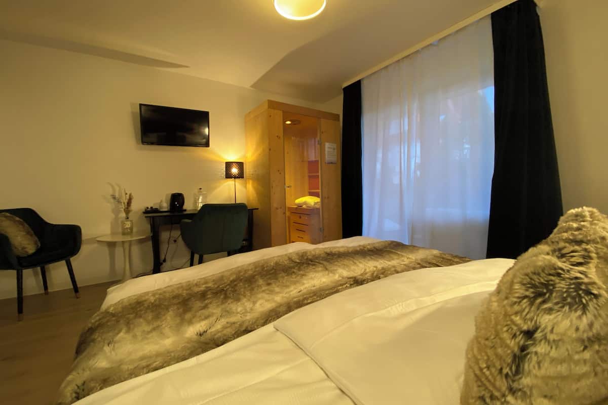 Habitación de hotel con cama, escritorio, silla, televisor y ventana con cortinas.